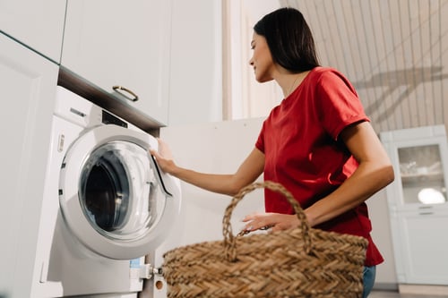 young-woman-putting-clothes-at-washing-machine-whi-2023-11-27-04-52-49-utc